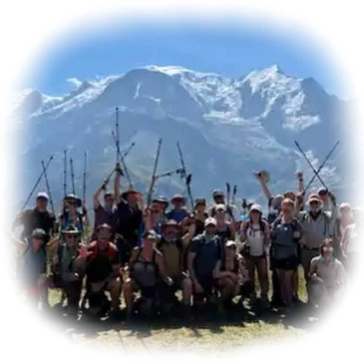 A group of hikers posing with trekking poles in front of snowy mountains under a blue sky.