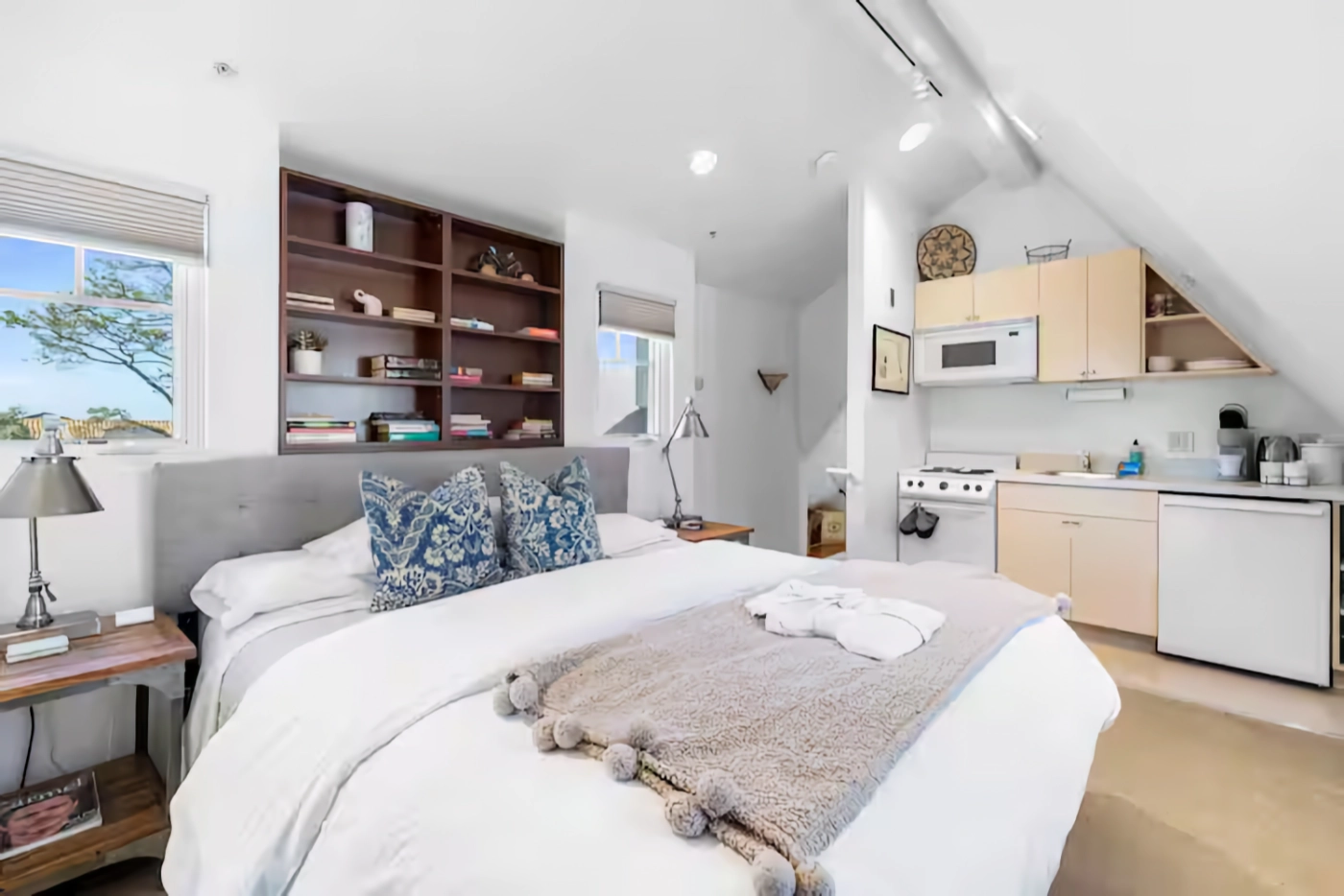 A studio apartment with a bed, bookshelf, and small kitchenette.